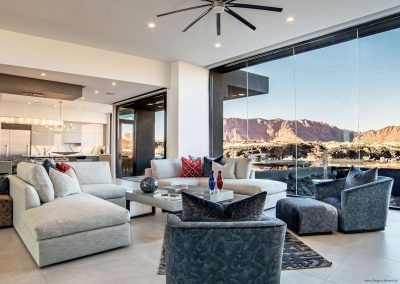A modern contemporary living room with floor to ceiling windows, sleep couches and chairs in shades of grey, angular designs, and pops of red and blue accent decor.