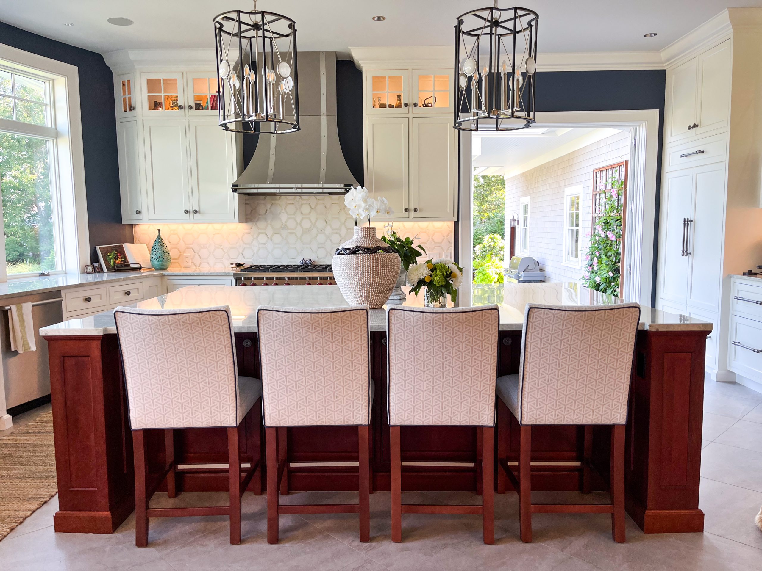 A bright kitchen with a cherry wood island and white upholstered chairs.