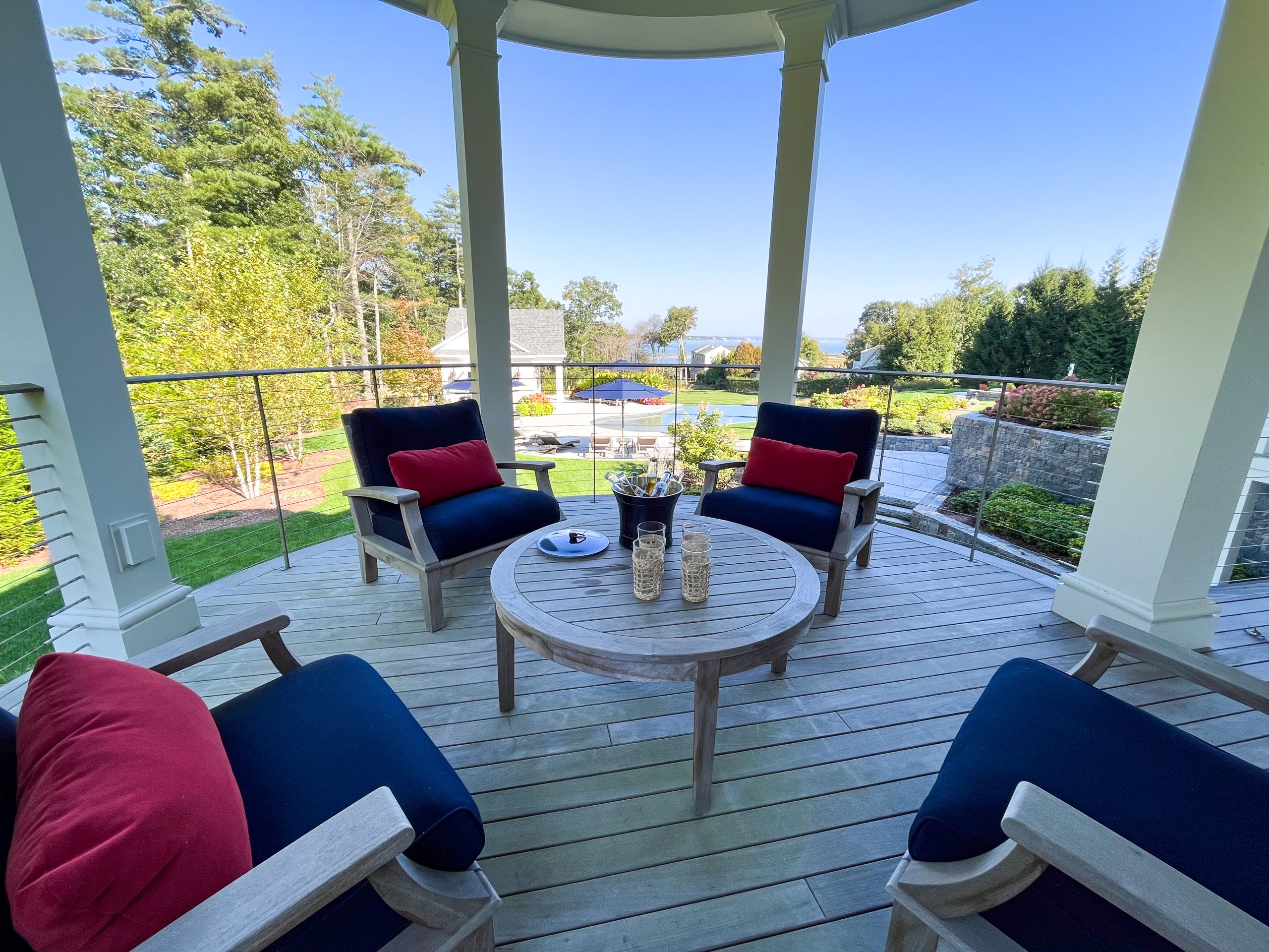 A round covered deck with a beautiful view and teak outdoor furniture with navy upholstery and red accent cushions. 