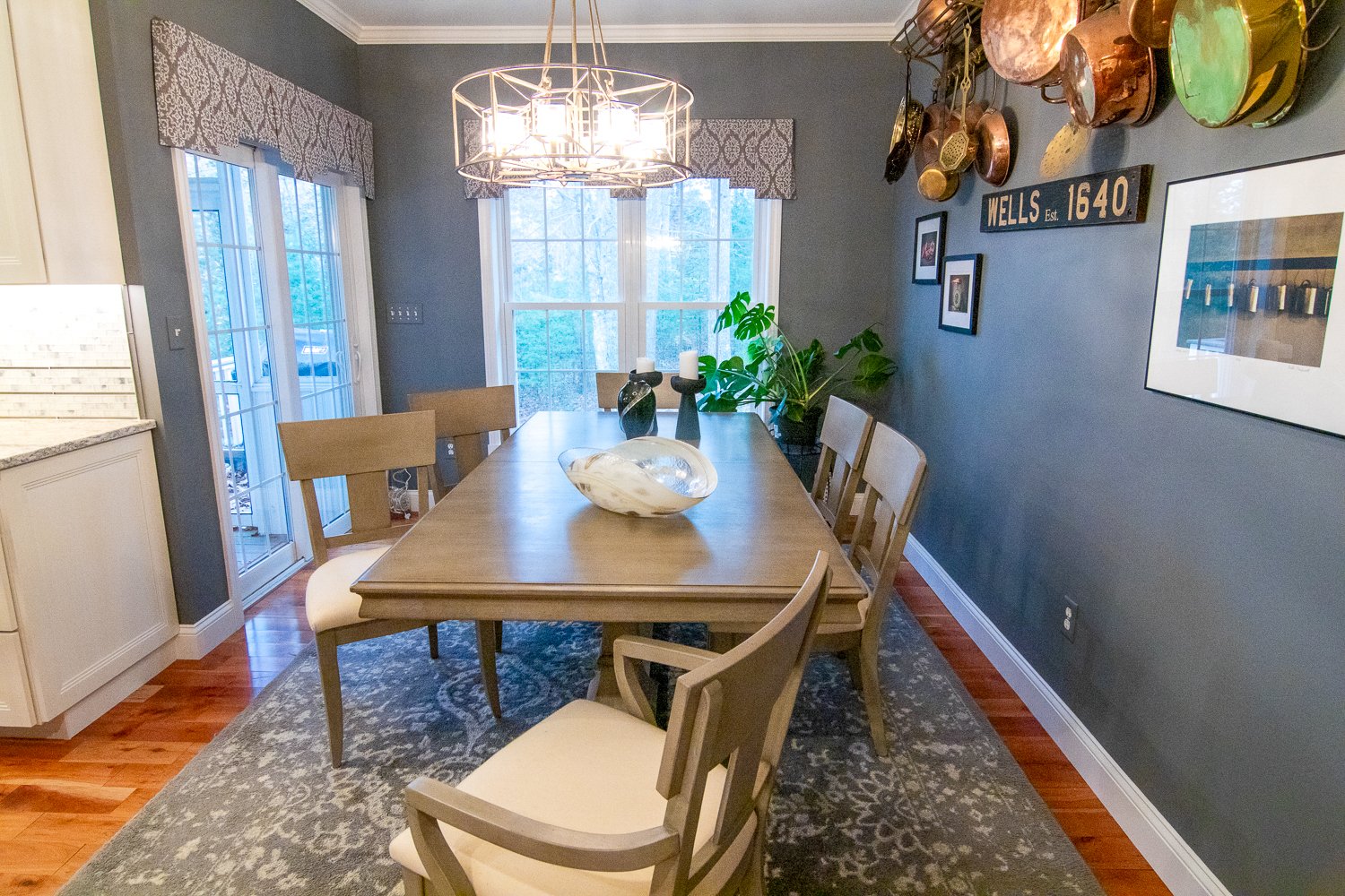 A dining room with greyish blue walls, a blue rug, a farmhouse style table and copper pots hanging on the walls